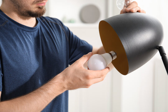 Man changing incandescent light bulb for fluorescent one in lamp at home, closeup - Powered by Adobe