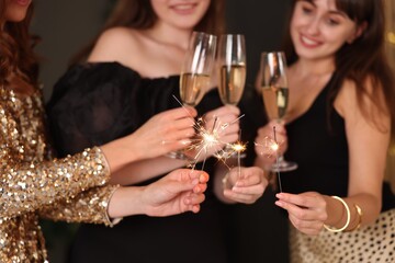 Women celebrating New Year with sparklers and wine glasses indoors, closeup