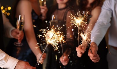 Friends celebrating New Year with sparklers and wine glasses indoors, closeup