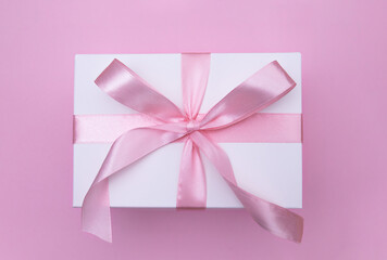 Top view of white gift box with pink ribbon on pastel pink background. Concept of celebration, birthday, gift giving.