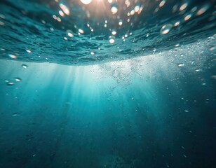 Obraz premium Underwater scene with sunlight rays shining through clear blue ocean water. Air bubbles rise from the depth to the surface creating a textured background.