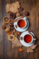 Aerial view of two cups of tea with cinnamon on a table with nuts and autumn leaves, vertically, with copy space