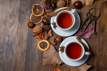 Aerial view of two cups of tea with cinnamon on a table with nuts, keys, and autumn leaves, horizontal, with copy space