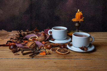 View of two cups of tea on a wooden table with nuts, leaves, keys, and a lit candle, horizontally with copy space