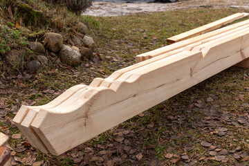 Wooden construction beams with decorative cut edges placed on ground at building site, detail of carpentry work, sustainable material for eco friendly house, timber structure element for architecture