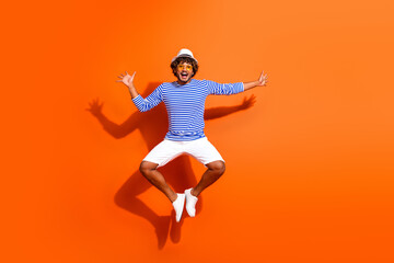 Happy young man jumping in sailor striped shirt on orange background showcasing summer fun and stylish casual fashion