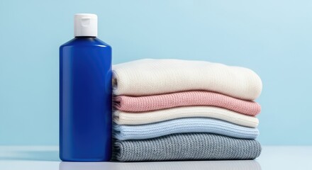 Stack of folded colorful knit sweaters and blue laundry detergent bottle set on a bright white surface with light blue backdrop and soft textures