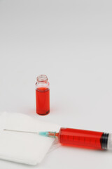 Glass ampoules with red vitamin B12 and a full syringe placed on a white surface symbolizing healthcare and treatment.