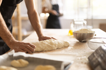 Elderly male baker preparing raw yeast dough on kitchen table in bakery