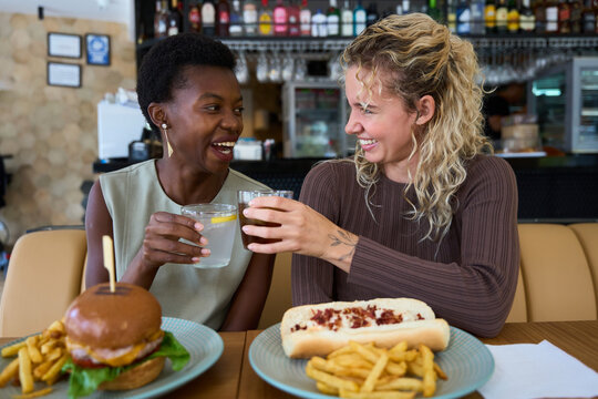 Diverse women friends toasting drinks laughing in restaurant - Powered by Adobe