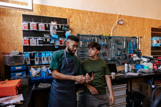 Mechanic teaching apprentice using phone in bike shop