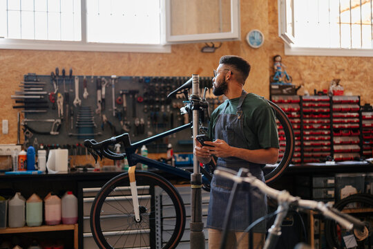 Mechanic man using phone working in bicycle workshop