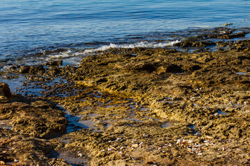 Rugged Coastal Rocks By Calm Blue Water With Weathered Stone Pier And Small Post