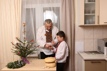 A man in Ukrainian embroidery and his son decorate a Christmas tree.
