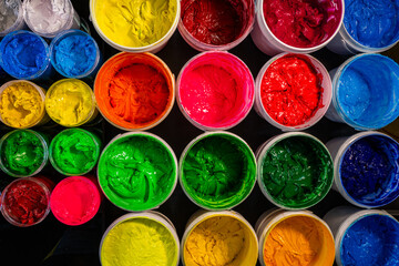 Colorful Ink for Screen Printing FactoriesInside a busy Tee shirt factory plastisol inks in multiple tones bright and dark are neatly arranged for industrial use. Workers use handmade tools handles