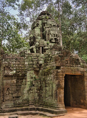 Bayon Faces in the Jungle - A close-up of two weathered, moss-covered stone faces carved into the ancient temple ruins, surrounded by lush jungle.