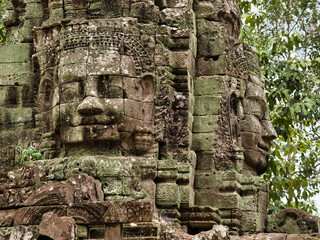 Khmer Smiling Stone Face - A close-up of a weathered, smiling stone face carving on a historic temple at Angkor, with detailed features and textures.