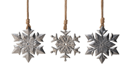 Three pressed-tin snowflake ornaments in matte nickel with burnished edges on linen cords isolated on transparent background.
