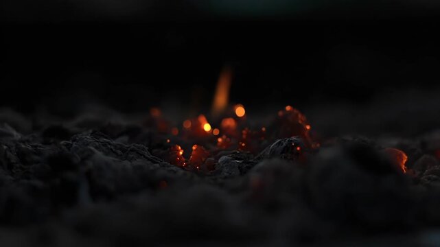 Close-up of glowing embers and ash, symbolizing warmth, destruction, and the aftermath of a fire, with a shallow depth of field creating a dramatic and moody atmosphere