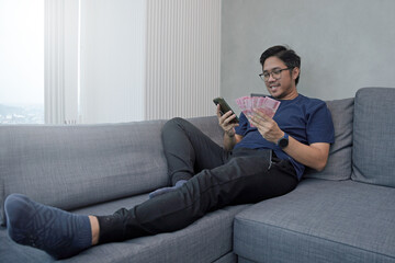 Obraz premium Asian young man holding Rupiah banknotes showing fist appreciating the joy of getting money. THR