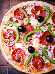 Pizza with chorizo ​​sausage, mozzarella cheese, green pepper and black olives. Rustic wooden background. Soft focus.	