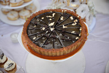 Chocolate pie topped with gold flakes and chocolate chunks is neatly sliced and displayed at a dessert table