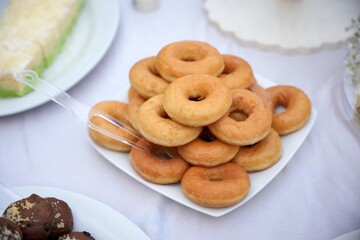 A stack of plain donuts is neatly arranged on a white square plate and displayed on the dessert table.
