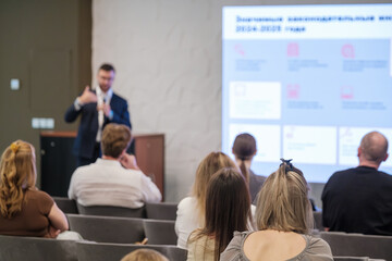 Presenter speaks to audience in conference room with projected slides showcasing topics and ideas