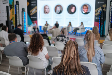 Fototapeta premium Audience attends conference panel discussion with speakers on stage in modern venue, bright screens, blue lighting