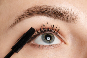 Obraz premium Woman applying mascara onto her eyelashes, closeup