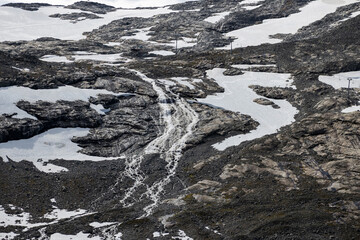 Fototapeta premium Majestic mountain scenery featuring rocky terrain, melting snow, and a powerful flowing waterfall