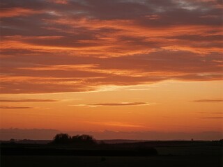 Vibrant orange and red sunset over a flat landscape with silhouetted trees and distant horizon