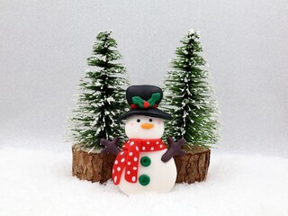 A snowman and two Christmas trees against a snowy background. Christmas card with copy space. Christmas decoration.