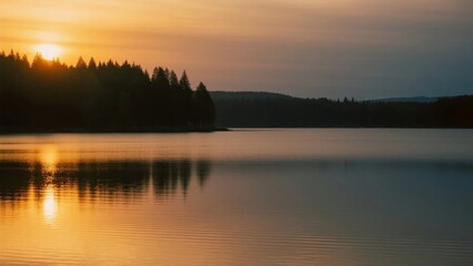 Fototapeta premium Sunset over a calm lake with forested shoreline and golden reflections