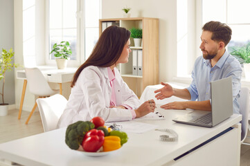 Nutritionist discusses plan for individual approach to nutrition with patient during consultation. Female doctor in medical office listens to man who consults about healthy eating habits.