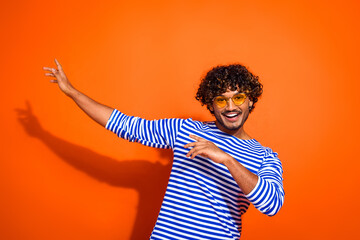 Excited young man in a striped sailor shirt gesturing cheerfully against an orange background...