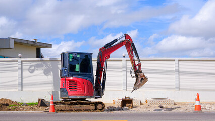 Excavator with crushing breaker is breaking concrete street floor in roadside area to carry out underground water pipe replacement work.