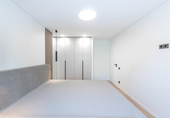 Wide Angle of Home Bedroom Interiom. King Size Double Bed and Wardrobe in Background. White Walls. Family Home. Closed White Wooden Door