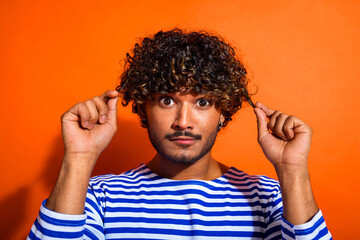 Funny stylish man with curly hair in striped sailor shirt posing playfully against a vibrant orange background with expressive gestures