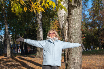 Cheerful joyful smiling mature adult woman walking in autumn park on a sunny day.