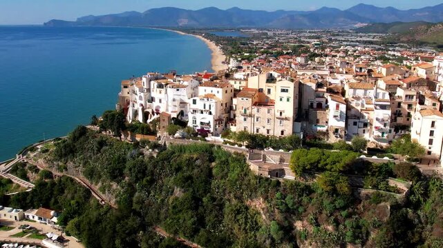 4K drone view of Sperlonga old town perched on the rocks. Aerial panorama of the iconic round shape bay, white sandy beach and turquoise Tyrrhenian Sea, Italy.