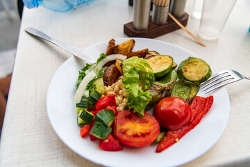 Tasty roasted peppers, tomatoes, and zucchini served with fresh green salad on a plate.