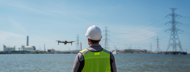 Engineer in a safety vest operating a drone to inspect and survey electrical power lines. Technician inspecting the power station for scheduled maintenance.