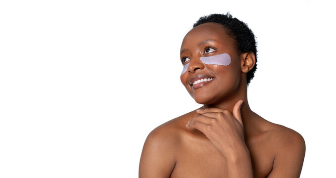 A woman wearing eye patches is smiling brightly against a clean, white background