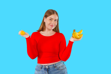 A woman wearing a vibrant red shirt is holding a bright yellow lemon in one hand and a bunch of...