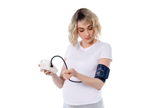 A pregnant woman is carefully monitoring her blood pressure at home using an electronic device