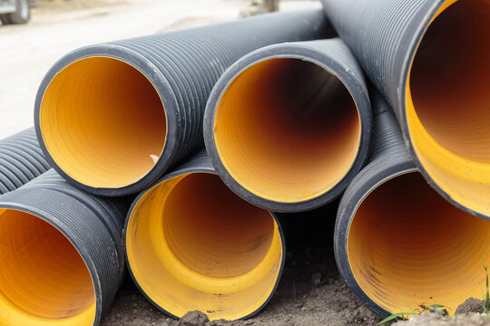 Black corrugated plastic drainage pipes with bright yellow interior stacked outdoors on a construction site for sewage, storm water, or cable protection