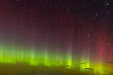 Green and red aurora lights shimmer across the star-filled night sky, creating a surreal and colorful celestial display above the horizon.