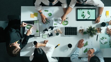 Top down view of business team discussing about using clean energy and sustainable investment at meeting table with wind mill, document with environmental graph and wooden house model. Alimentation.
