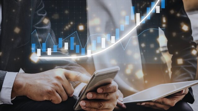 Two business professionals engage with a smartphone and tablet while examining financial charts and graphs that highlight market trends in a modern office environment. Copula